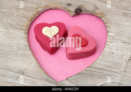 Herzförmige Petits Fours zum Valentinstag in einem Herz aus Holz Stockfoto