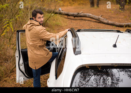 Junger Mann stand in der Nähe weißes Auto und großen umgestürzten Baum auf Waldweg am Herbsttag Stockfoto