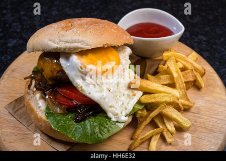 Hausgemachter Käse Burger mit Brot, Ei, Pommes Frites und Soße auf Holzplatte Stockfoto