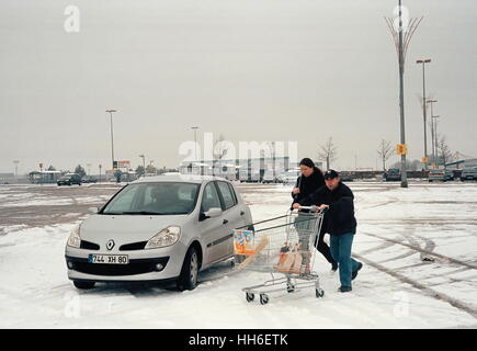 AJAXNETPHOTO. GLISY, FRANKREICH. -PAAR DRÄNGEN SHOPPING TROLLEY ÜBER SUPERMARKT AUTO PARKEN IM SCHNEE.  FOTO: JONATHAN EASTLAND/AJAX REF: TC6913 91202 8 5A Stockfoto