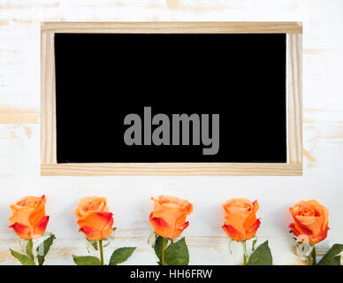 Orange Rosen auf weißem Holz Hintergrund und schwarze Tafel Stockfoto