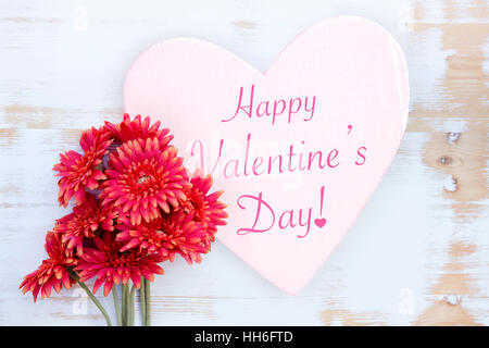 Rote Blumen auf weißem Holztisch mit Worten Happy Valentines Day geschrieben am Herz aus Holz Stockfoto