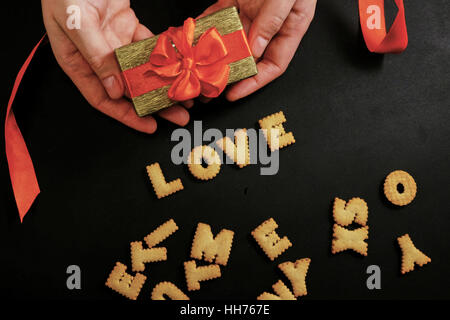 Zwei Hände halten ein Geschenk mit rotem Band mit Wort Liebe Stockfoto