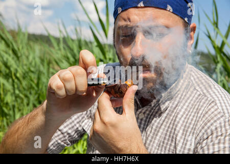 Bärtiger Mann, die Beleuchtung seiner Pfeife außerhalb an einem Sommertag Stockfoto