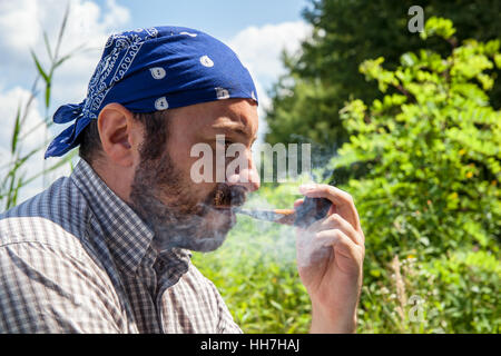 Bärtiger Mann raucht seine Pfeife und Freigabe Rauch außerhalb an einem Sommertag Stockfoto