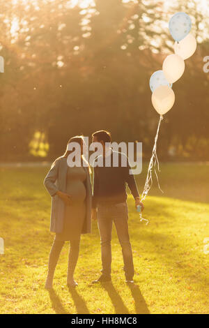 Junge schwangere Frau und Mann posiert im Herbst Park mit Luftballons in der hand Stockfoto