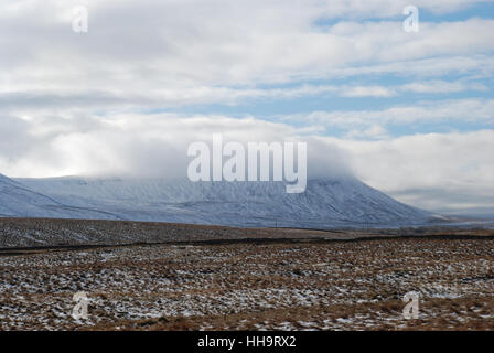 Die niedrige Wolke fließt im Winter über die Bergkuppe eines schneebedeckten Ingleborough Stockfoto