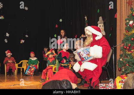 Kindergartenkinder als Elfen für Weihnachtsfeier erhalten Geschenke vom Weihnachtsmann verkleidet Stockfoto