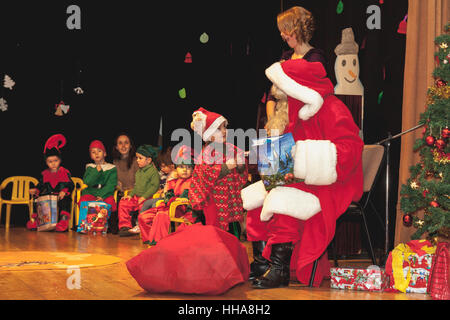 Kindergartenkinder als Elfen für Weihnachtsfeier erhalten Geschenke vom Weihnachtsmann verkleidet Stockfoto