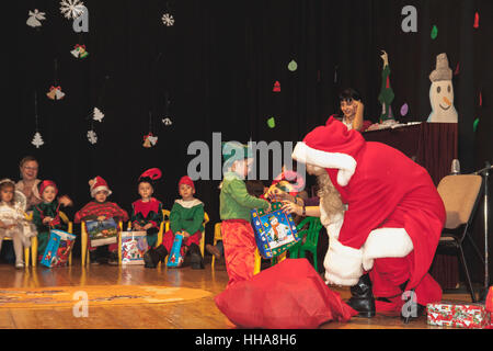 Kindergartenkinder als Elfen für Weihnachtsfeier erhalten Geschenke vom Weihnachtsmann verkleidet Stockfoto