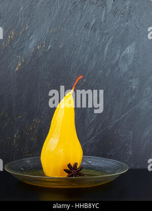 Einzelne Birne pochiert in Zucker und Safran Sirup gewürzt mit Sternanis auf einer Glasplatte mit grauem Schiefer Hintergrund Stockfoto