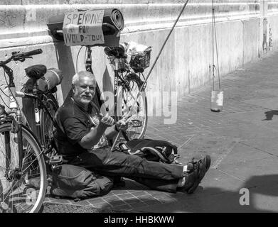 Mann liegt auf der Straße, schaut in die Kamera bitten um Geld für seine Reisen. Stockfoto