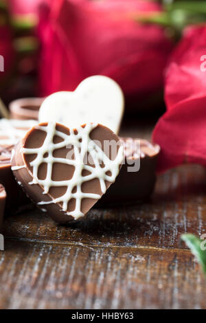 Nahaufnahme von Schokolade mit roten Rosen im Hintergrund in Herzform. Stockfoto