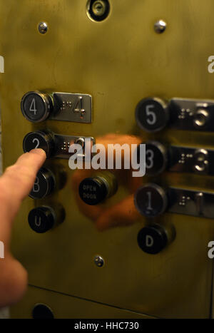 Ein Finger drückt auf den Boden-Button auf eine Messingplatte in einem alten Aufzug Stockfoto