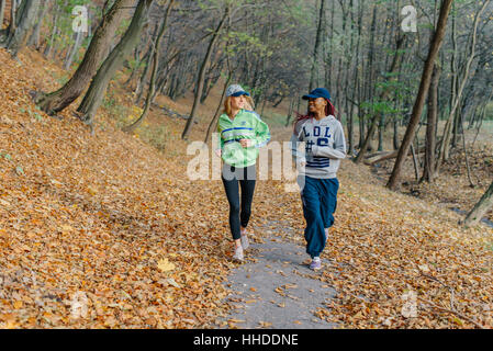 Zwei sportliche Frauen im Herbst Park Joggen. Blond und afrikanische Mädchen. Gelbe Blätter. Glücklicher Tag Stockfoto