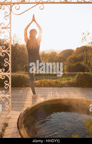 Frau praktizieren Yoga Baum darstellen auf Terrasse mit Whirlpool und Herbst Strukturansicht Stockfoto