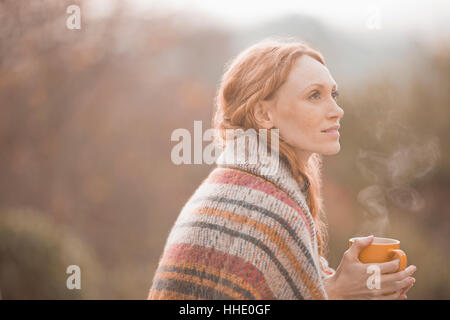 Gelassene Frau eingewickelt in Decke heißen Kaffee trinken im freien Stockfoto