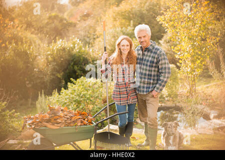 Porträt Ehepaar mit Hund im Garten Rechen Lächeln verlässt im Herbst Garten Stockfoto