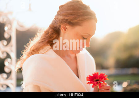 Heitere Frau mit roten Gerbera Daisy auf sonnigen Terrasse Stockfoto