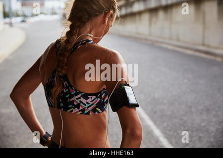 Fit weibliche Läufer in Sport-BH mit Armband für MP3-Player und Kopfhörer ruht auf städtischen Straße Stockfoto