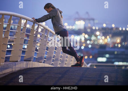 Weibliche Läufer dehnen Beine auf städtischen Steg im Morgengrauen Stockfoto