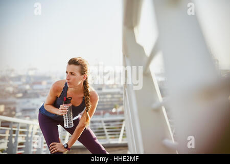 Weibliche Läufer Dehnung Bein und Trinkwasser auf sonnigen urban Steg ruht Stockfoto