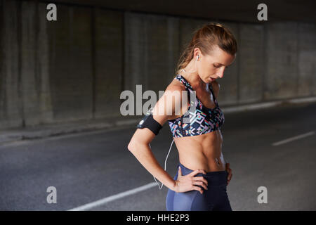 Fit weibliche Läufer in Sport-BH mit Armband für MP3-Player und Kopfhörer ruht in städtischen tunnel Stockfoto