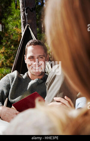 Zwei Menschen sitzen in Hängematten im Freien. Ein Mann, der lächelte eines Begleiters. Stockfoto