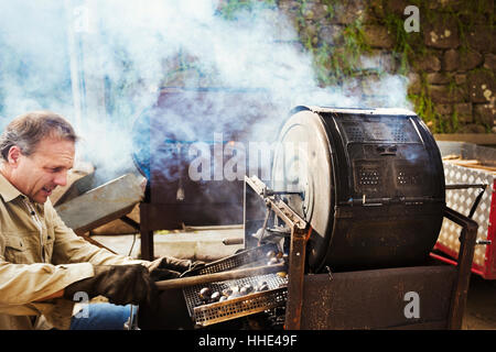 Ein Mann rösten Kastanien über glühende Kohlen in einer großen Trommel, Rechen, gerösteten Nüssen. Stockfoto