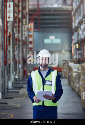 Porträt lächelnde Arbeiter mit Zwischenablage im Auslieferungslager Stockfoto
