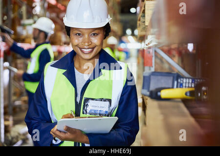 Porträt lächelnd Arbeitnehmerin mit Zwischenablage im Auslieferungslager Stockfoto