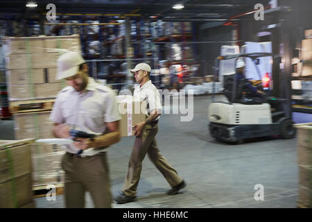 Arbeiter tragen und Umzugskartons mit Gabelstapler im Auslieferungslager Laderampe Stockfoto