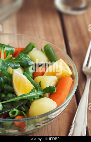 Salat mit Baby-Karotten, Erbsen, Zwiebeln und Kartoffeln in Glasschüssel auf hölzernen Hintergrund Stockfoto