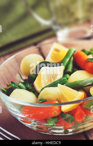 Salat mit Baby-Karotten, Erbsen, Zwiebeln und Kartoffeln in Glasschüssel auf hölzernen Hintergrund Stockfoto