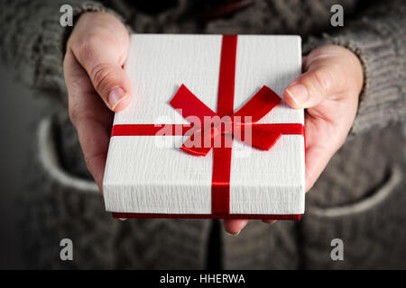 Weibliche Hände halten eine Geschenkbox mit rotem Band. Hautnah. Stockfoto