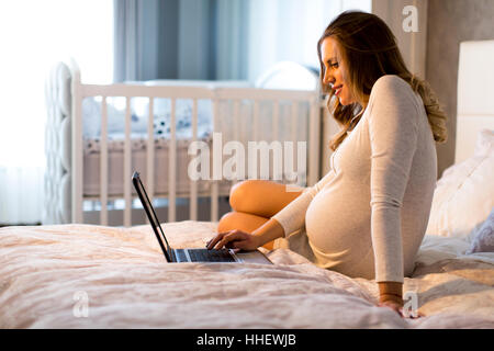 Hübsche junge schwangere Frau arbeiten am Laptop im Bett Stockfoto