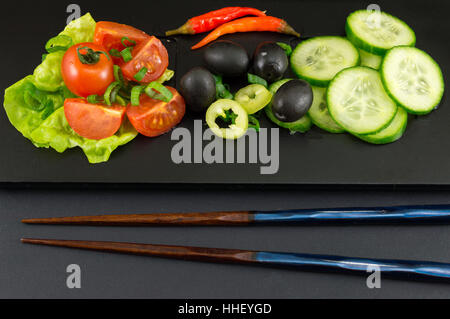 Ess-Stäbchen und Gemüsesalat auf schwarzem Hintergrund Stockfoto