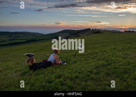 Hund und Mädchen entspannt den Sonnenuntergang in einem Feld auf einem Hügel Stockfoto