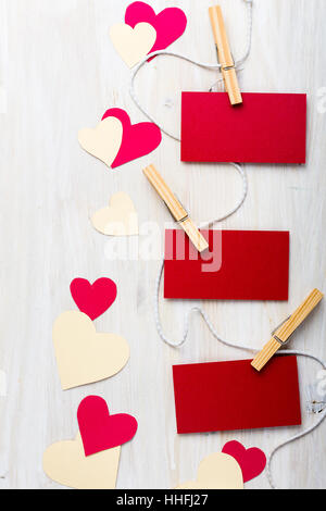 Drei rote Papierherzen und Blatt hängen string mit Mini-Wäscheklammer über hölzerne Tafel. Draufsicht mit Textfreiraum Stockfoto