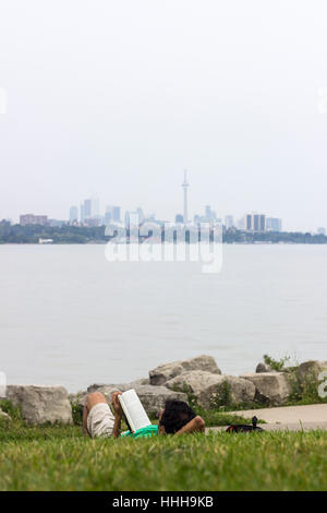 Mann auf den Rasen legen und lesen Sie ein Buch mit einem Toronto Skyline im Hintergrund Stockfoto