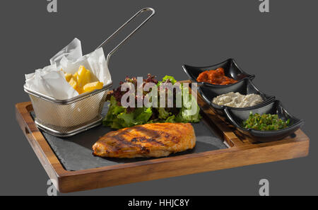 Huhn gebraten mit einer Seitenlänge von Pommes Frites mit drei Arten von Soße serviert in einer Schale aus Holz und Stein Stockfoto