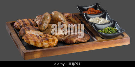 verschiedene Grilladen mit drei Arten von Soße serviert in einer Schale aus Holz und Stein Stockfoto