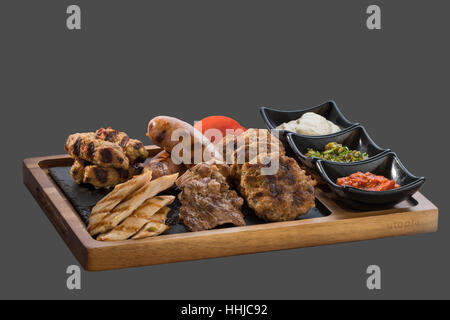 verschiedene Grilladen mit drei Arten von Soße serviert in einer Schale aus Holz und Stein Stockfoto