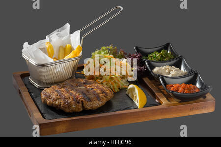 Frikadelle aus Fleisch garniert mit Kraut und Bratkartoffeln mit drei Arten von Sauce mit dreierlei Gericht in Holz und Stein Stockfoto