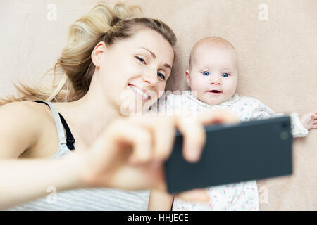 Mutter und Säugling Baby nehmen Selfie mit Telefon im Bett Stockfoto