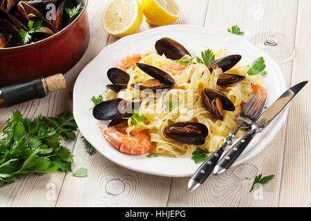 Pasta mit Meeresfrüchten und Weißwein auf Holztisch. Muscheln und Garnelen Stockfoto