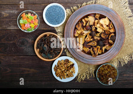 Getrocknete Früchte (Äpfel, Birnen, Aprikosen), Beeren, Walnuss-Kerne, Rosinen, Mohn in einer Schüssel auf dunklem Holz. Stockfoto