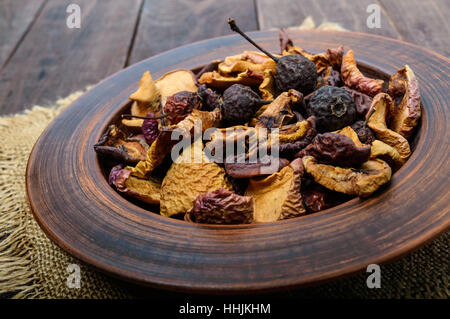 Getrocknete Früchte (Äpfel, Birnen, Aprikosen), Beeren in einer Schüssel auf dunklem Holz. Hautnah. Zutaten für den Winter Vitamindrink, Kompott. Stockfoto