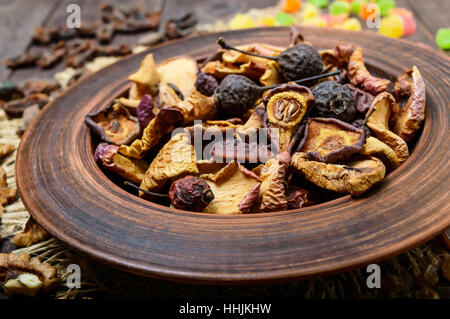 Getrocknete Früchte (Äpfel, Birnen, Aprikosen), Beeren, Rosinen und Nüssen in einer Schüssel auf dunklem Holz. Hautnah. Stockfoto