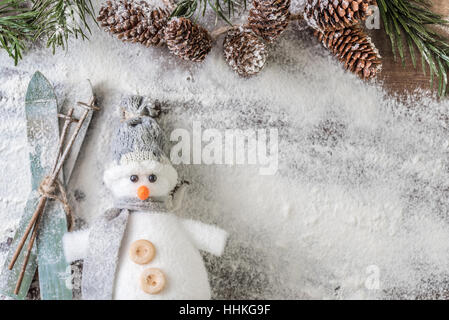 grau-weißer Schneemann mit ein Paar Skier und einen verschneiten Tannen Zweig mit Zapfen auf weißem Hintergrund Stockfoto